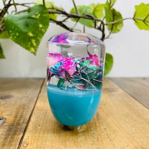 May include: A clear glass gear shift knob with a teal blue base and preserved flowers inside. The flowers are pink, purple, and white.
