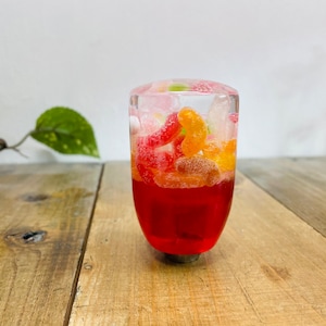 Può includere: Un pomello del cambio in resina trasparente riempito di caramelle gommose rosse e gialle. Il pomello è rotondo e ha una base argentata.