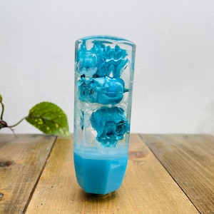 Op de afbeelding: Een transparante blauwe hars versnellingspookknop met geconserveerde blauwe bloemen erin.
