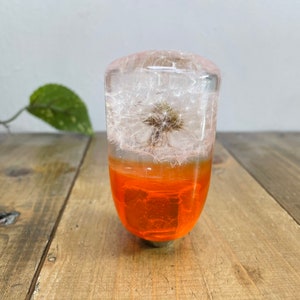 May include: A clear resin gear shift knob with a dandelion flower encased inside. The bottom of the knob is a bright orange color.