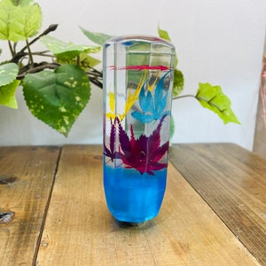 May include: A clear glass gear shift knob with a blue base and colourful pressed flowers inside. The flowers are yellow, red, and purple.