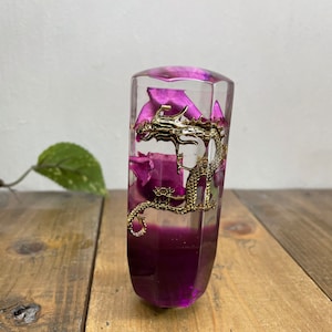 Op de afbeelding: Een transparante glazen versnellingspookknop met een gouden draak en paarse hars erin.