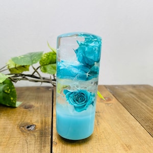 May include: A clear glass cylinder containing a blue and white floral arrangement. The cylinder is resting on a wooden surface.