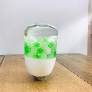 以下が含まれることがあります： 白いベースと緑と白の装飾要素が内側に施された透明なガラス製のシフトノブです