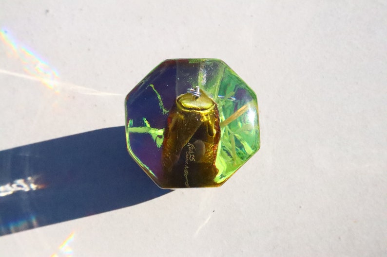 May include: A green, octagonal, glass paperweight with a gold beetle encased inside. The beetle has a label that reads "Realis - Ecuador".