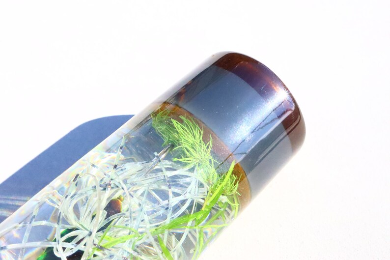 May include: A clear glass tube with a brown and silver top, filled with green and white plant material.