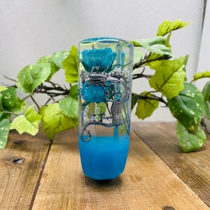 Pode incluir: Uma alavanca de câmbio de resina azul com uma libélula prateada e flores azuis dentro.