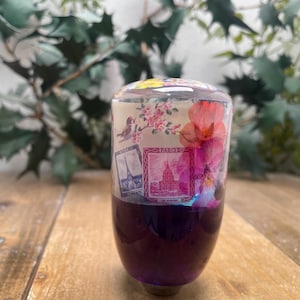 Peut inclure: Un pommeau de levier de vitesse en verre transparent avec une base violette. Le pommeau présente un motif floral avec des fleurs roses et rouges, et un motif de timbre vintage avec le mot "Paris" imprimé dessus.