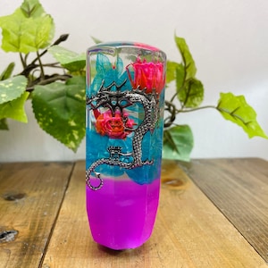 May include: A clear resin gear shift knob featuring a silver dragon design and pink and blue flowers encased within. The base of the knob is a vibrant purple colour.