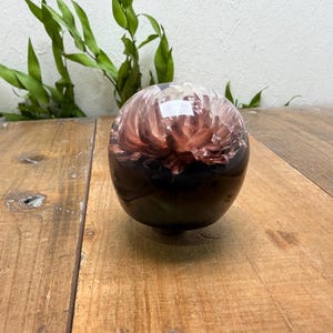May include: A clear, spherical decorative object with a dark base and a floral design in shades of brown and white. The object is sitting on a wooden surface.