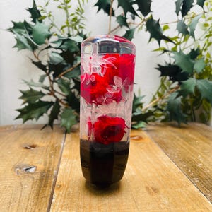 Könnte beinhalten: Ein transparenter Glas-Schalthebelknauf mit roten und weißen gepressten Blumen im Inneren. Die Blumen sind in einem vertikalen Muster angeordnet.