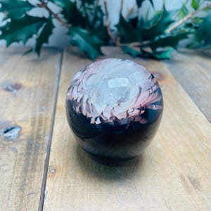 May include: A black and white crystal sphere with pink and white inclusions. The sphere is smooth and polished.