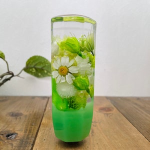 May include: A clear green glass gear shift knob with white and green pressed flowers inside. The knob has a green base.