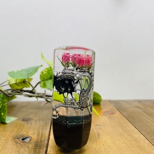 Op de afbeelding: Een transparante resin versnellingspookknop met een zwarte basis. Binnen in de knop bevinden zich roze bloemen en een zilveren metalen draak.