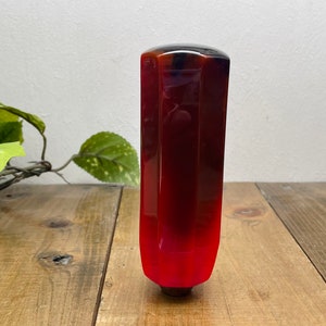 May include: A red, black and white resin gear shift knob with a geometric shape.