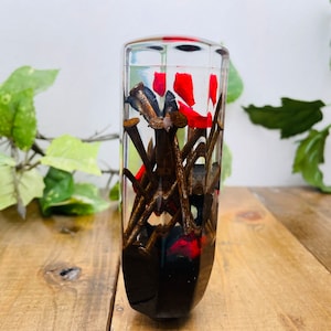 Op de afbeelding: Een transparante glazen cilinder gevuld met roestige spijkers en rode hars. De cilinder heeft een afgeronde boven- en onderkant.