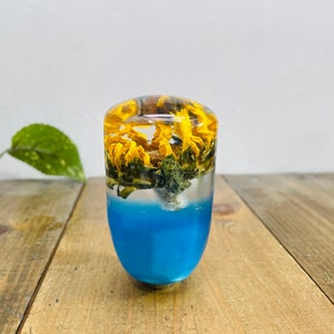 May include: A clear resin gear shift knob with yellow dried flowers and a blue resin base.