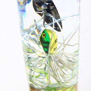 May include: A green and yellow fishing lure with white and silver fishing line in a clear glass. The lure has a black eye and the text "F 3/8" on the side.