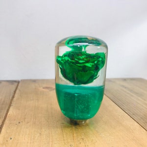 Puede incluir: Un pomo de palanca de cambios decorativo con una rosa verde incrustada en resina transparente y una base verde.