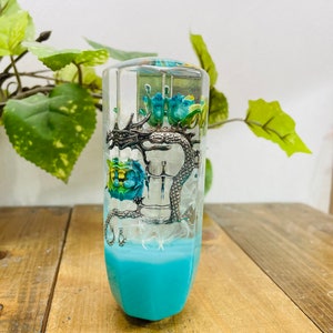 Pode incluir: Uma alavanca de câmbio de vidro transparente com um dragão prateado e flores azuis e verdes dentro. A alavanca tem uma base azul.