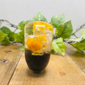 Op de afbeelding: Een transparante resin versnellingspookknop met gele en witte geperste bloemen erin. De knop heeft een zwarte basis.