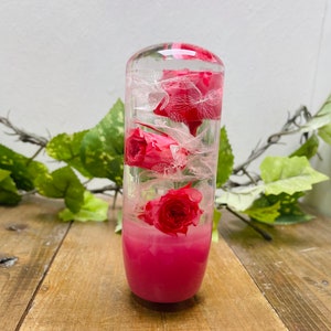 Könnte beinhalten: Ein rosafarbener Schaltknauf aus Harz mit echten gepressten Blumen im Inneren. Die Blumen sind rosa und weiß und durch das klare Harz sichtbar.