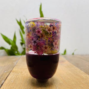 Könnte beinhalten: Dekorativer Schalthebelknauf mit einem transparenten Harzaufsatz, der mit bunten Trockenblumen gefüllt ist. Die untere Hälfte ist tief burgunderfarben. Der Knauf ist für den Schalthebel eines Autos bestimmt.