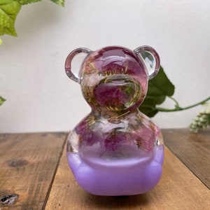 May include: A clear resin bear figurine with purple flowers encased inside. The bear is sitting on a purple base.