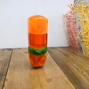 Peut inclure: Une barre de savon orange et verte en couches sur une surface en bois.