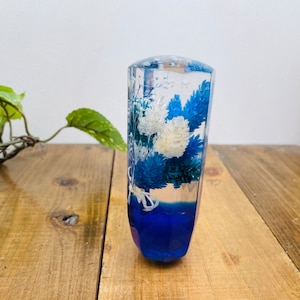 May include: A clear resin gear shift knob with blue and white pressed flowers inside. The knob has a blue base.