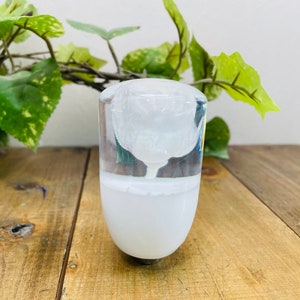 Könnte beinhalten: Ein durchsichtiger Glasflaschenverschluss mit einer weißen Rose im Inneren. Die Rose ist teilweise durch das Glas sichtbar.