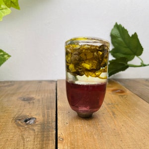 Op de afbeelding: Een transparante glazen pookknop met een rode basis en gedroogde gele bloemen erin.