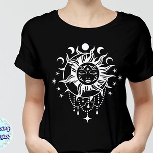 K&ouml;nnte beinhalten: Ein schwarzes T-Shirt mit einem wei&szlig;en Sonnen- und Monddesign. Die Sonne hat ein Gesicht mit geschlossenen Augen und ist von einem Halbmond und Sternen umgeben.