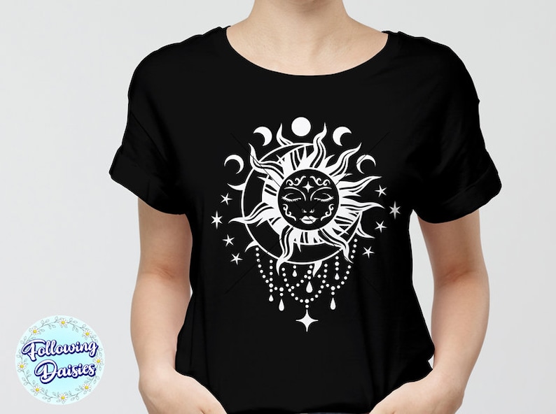 K&ouml;nnte beinhalten: Ein schwarzes T-Shirt mit einem wei&szlig;en Sonnen- und Monddesign. Die Sonne hat ein Gesicht mit geschlossenen Augen und ist von einem Halbmond und Sternen umgeben.