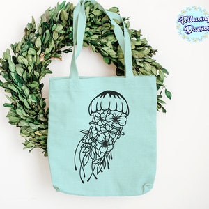 May include: A light blue tote bag with a black floral jellyfish design. The bag has two handles and is made of a soft, canvas-like material.