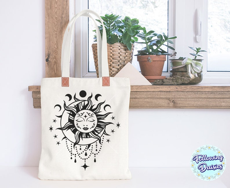 K&ouml;nnte beinhalten: Eine wei&szlig;e Einkaufstasche mit einer schwarz-wei&szlig;en Illustration einer Sonne und eines Mondes mit einem Gesicht. Die Sonne hat ein geschlossenes Auge und ein kleines L&auml;cheln. Die Einkaufstasche hat braune Ledergriffe.