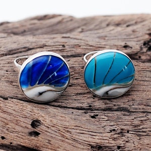 May include: Two silver rings with blue and turquoise inlays. The rings have a round design with a white centre and blue or turquoise outer edges.
