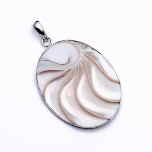 Puede incluir: Un colgante de plata con una concha de nautilus blanca con un patrón de remolino. La concha tiene forma ovalada y un acabado liso y pulido.