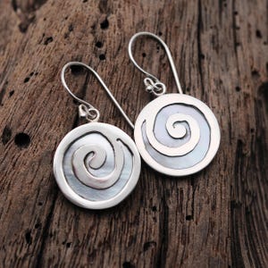 May include: Silver earrings with a white mother of pearl inlay featuring a spiral design.