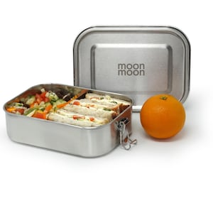 May include: A stainless steel lunch box with a latch closure. The lunch box is divided into two compartments and contains a salad and sandwiches. The lid of the lunch box has the words "moon moon" printed on it.