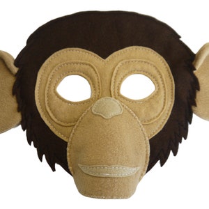 May include: A felt monkey mask in shades of brown and beige. The mask has eye holes, a nose, and a stitched mouth, with attached ears. The mask is designed for costume use or imaginative play. The mask is made from soft felt material.