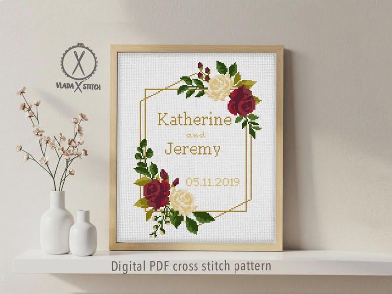 May include: A cross stitch pattern in a light wood frame featuring a gold geometric border, red and cream roses, green leaves, and the text Katherine and Jeremy 05.11.2019. The logo VLADA STITCH is visible in the upper left corner of the design.