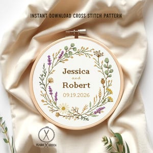 Può includere: Un modello a punto croce in un telaio da ricamo in legno. Il design presenta una ghirlanda floreale con i nomi "Jessica e Robert" e la data "09.19.2026". Il testo "INSTANT DOWNLOAD CROSS STITCH PATTERN" è in alto.