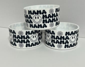 May include: Three white ceramic cups with black and white designs. The cups have a repeating pattern of the word "mama", smiley faces, and flowers.