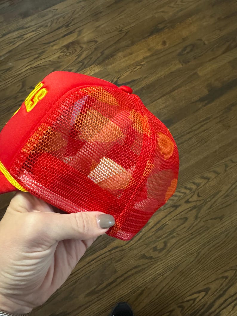 May include: Red and yellow mesh trucker hat with a yellow logo. The logo is a stylized letter "S" with a yellow outline.
