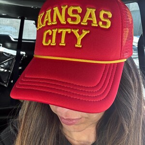 May include: Red trucker hat with a yellow embroidered logo that says "KANSAS CITY".