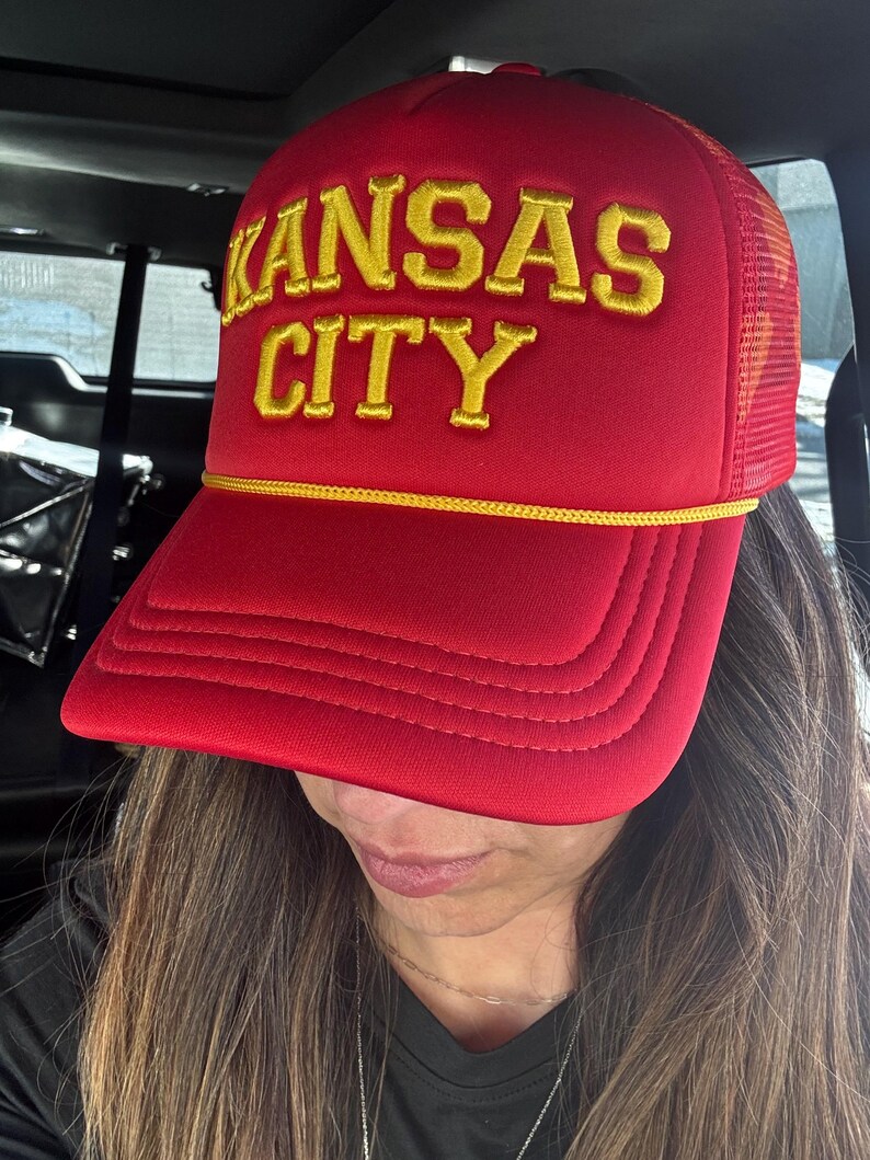 May include: Red trucker hat with a yellow embroidered logo that says "KANSAS CITY".