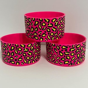 Op de afbeelding: Drie roze siliconen onderzetters met een zwart en geel luipaardmotief.