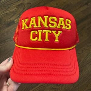 May include: Red trucker hat with a yellow embroidered logo that says "KANSAS CITY"