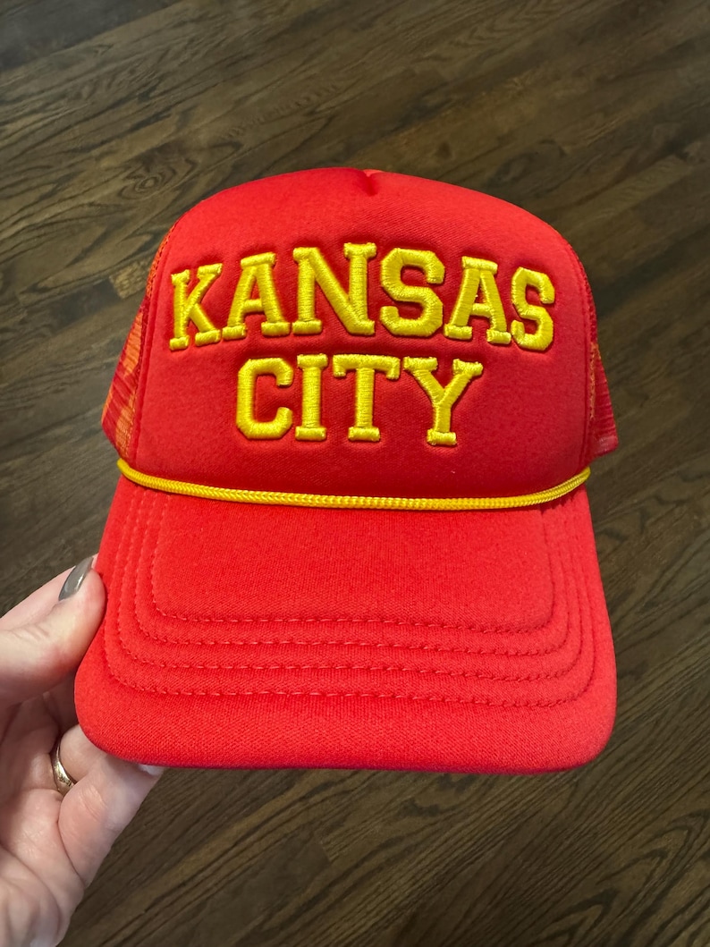 May include: Red trucker hat with a yellow embroidered logo that says "KANSAS CITY"